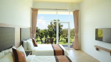 A hotel room with two beds, a TV, and a balcony with a view of trees.