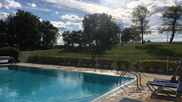 Una piscina con agua azul cristalina, rodeada por una zona verde con árboles y una valla.