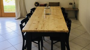 Un comedor con mesa de madera, sillas negras, lámpara colgante y vistas al exterior a través de un ventanal.