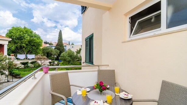 A balcony with a table set for breakfast, including plates, cups, and a vase of flowers.