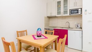A compact kitchen with white cabinets, a microwave, a kettle, and a small refrigerator.