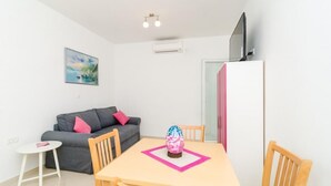 A compact living space with a dining table, a gray sofa with pink cushions, a small white table, and a pink decorative item on the table.