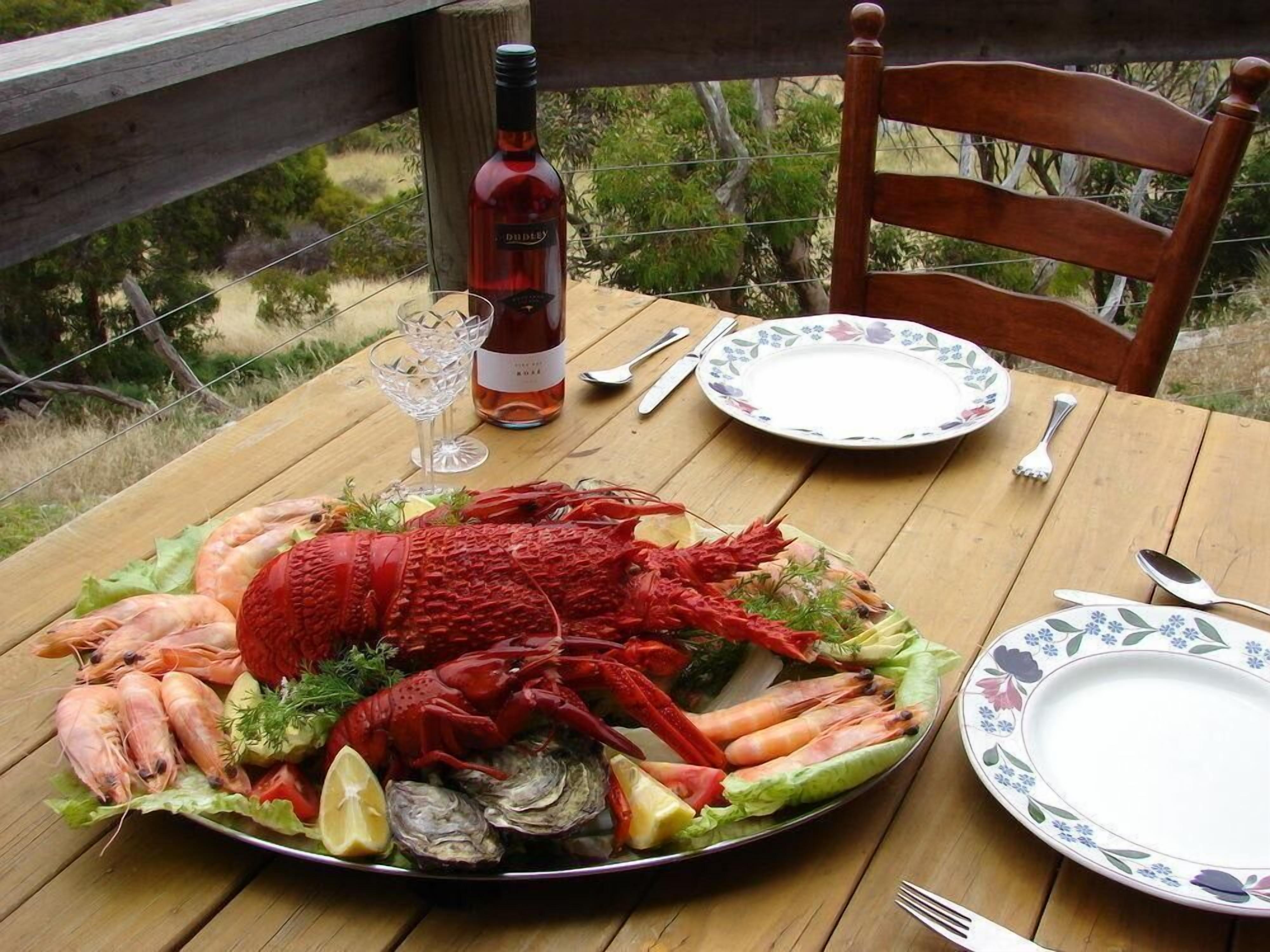 Tavolo apparecchiato all'aperto con un piatto di pesce, una bottiglia di vino e un piatto decorato con fiori.