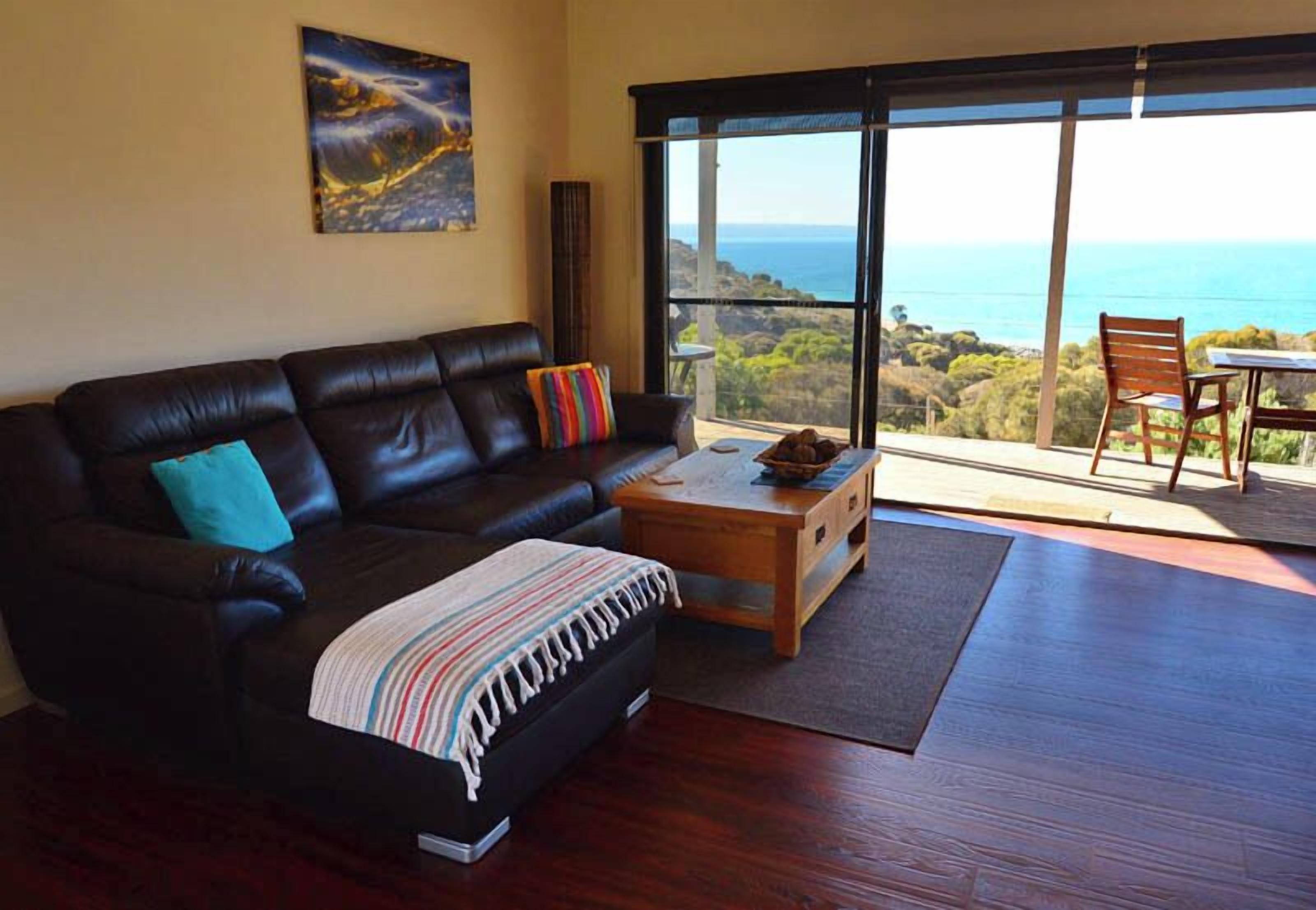 A living room with a dark leather sofa, a wooden coffee table, and a view of the ocean through large sliding doors.