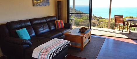 A living room with a dark leather sofa, a wooden coffee table, and a view of the ocean through large sliding doors.