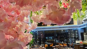 An indoor seating area with leather sofas and tables, surrounded by pink flowers. - XQ Pattaya Hotel (Pattaya)