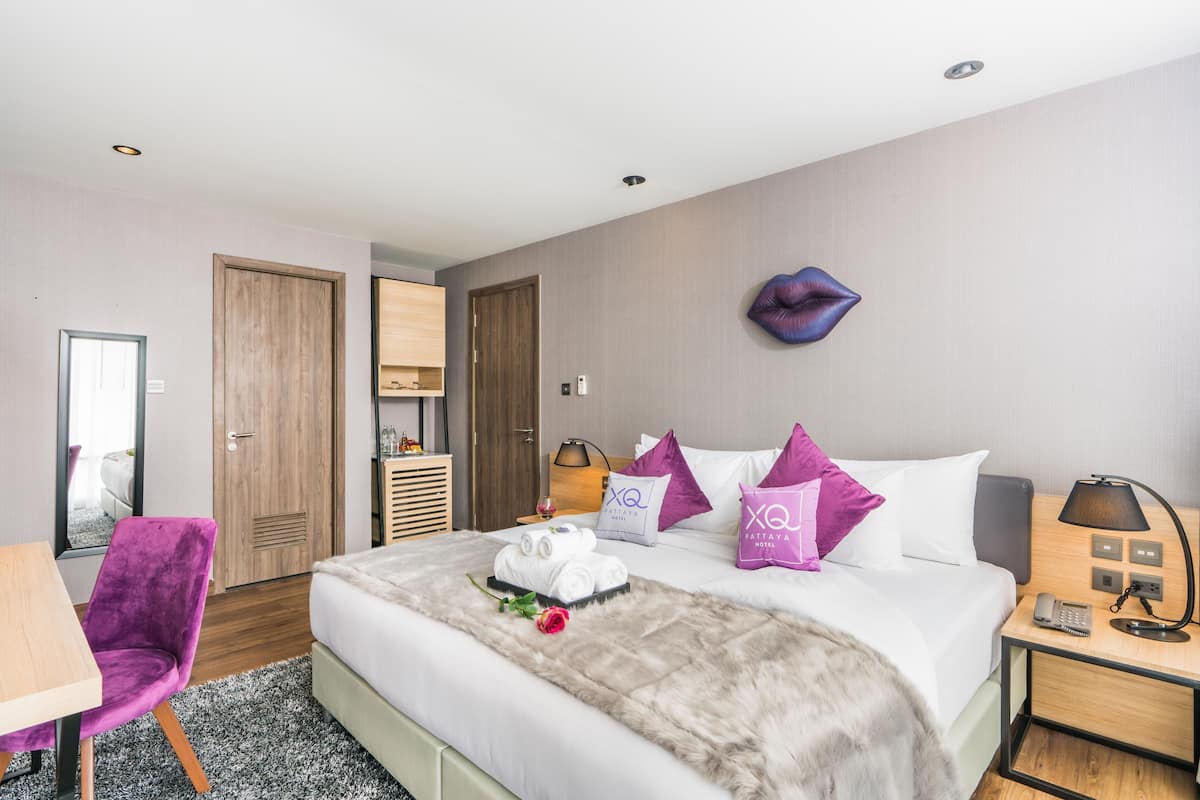 A hotel room with a large bed, a desk, a chair, and a wardrobe.