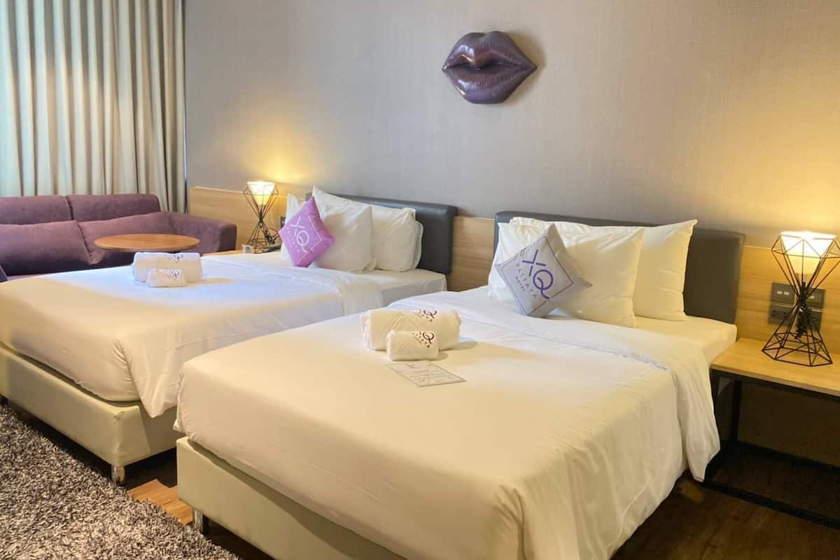 A hotel room with two beds, a sofa, a wall-mounted heart-shaped decoration, and bedside lamps.
