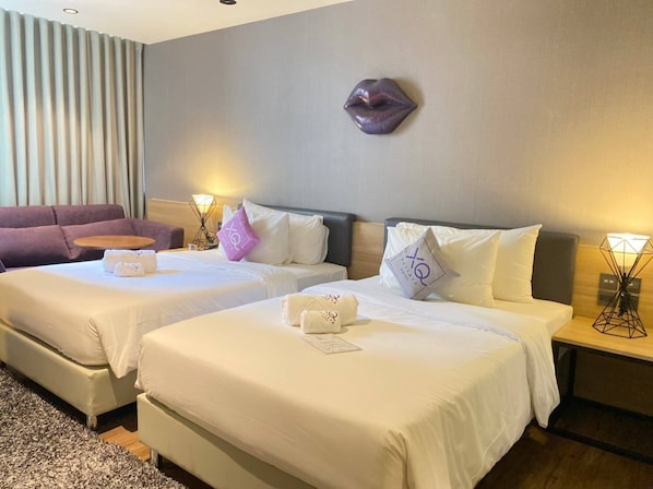 A hotel room with two beds, a sofa, a wall-mounted heart-shaped decoration, and bedside lamps. - XQ Pattaya Hotel (Pattaya)