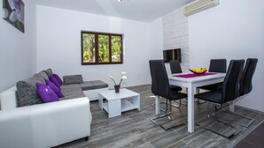 A modern living room with a white sofa, a coffee table, and a dining area with a white table and black chairs. - Villa Roza- Two-Bedroom Apartment (Mokosica)