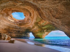 En naturlig klippformation med en stor öppning, en sandstrand och havet synligt genom öppningen.