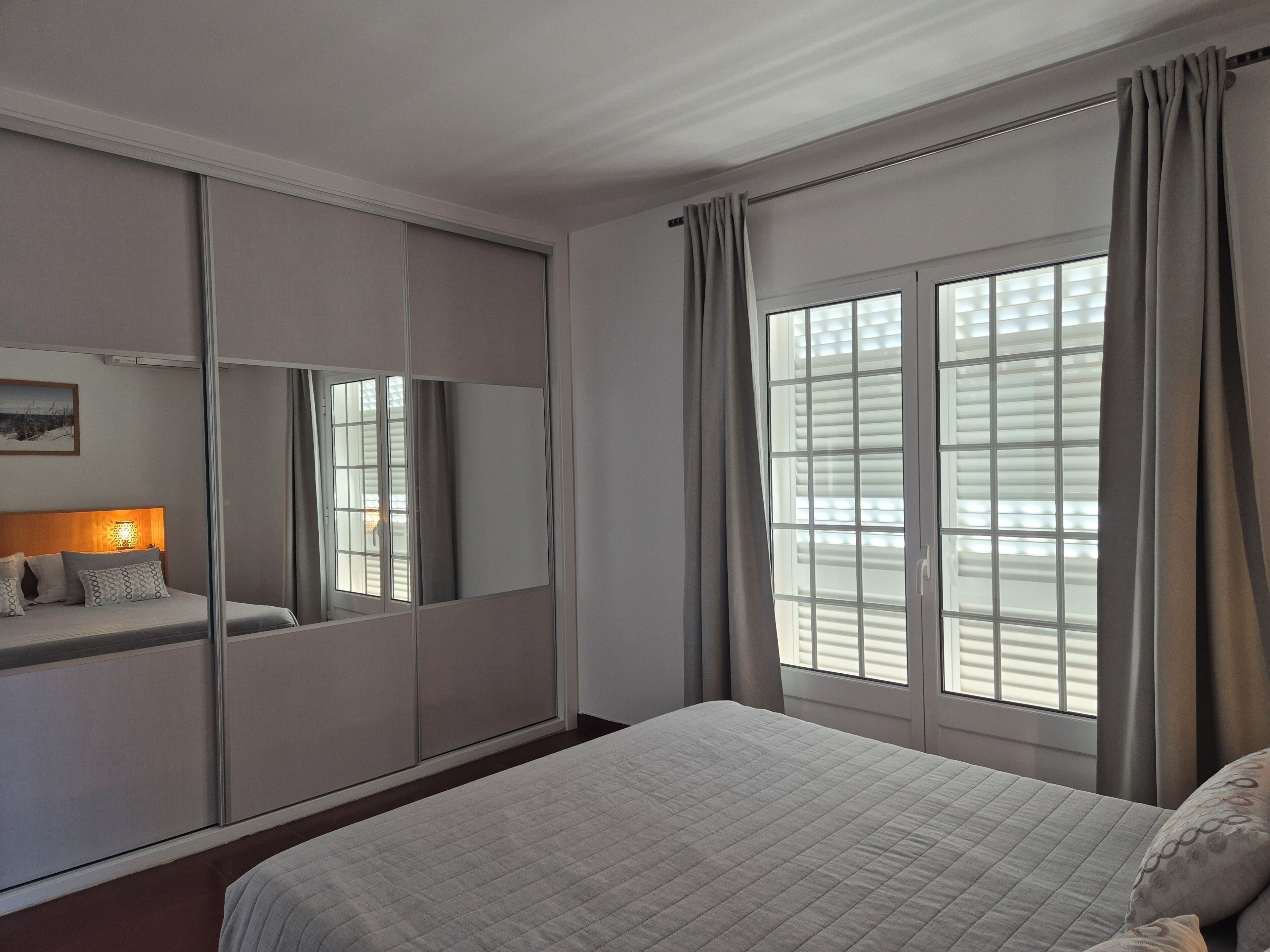 A hotel room with a bed, a wardrobe, a mirror, and a window with curtains.