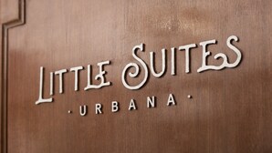 Une porte en bois sur laquelle est gravée l’inscription « Little Suites Urbana ».