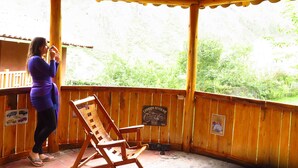 Eine überdachte Holzterrasse mit einem Holzstuhl und einer Person, die ein Mobilgerät benutzt.