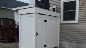 A white utility shed with a door and windows, located on a gravel driveway next to a house with a wooden staircase and a window. - Newly renovated family home 11/2 blocks from the beach and town center (Sea Isle City)