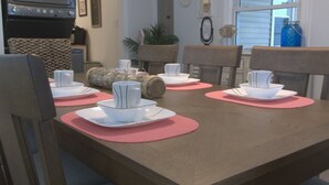 A dining table set with white plates, bowls, and cups, surrounded by chairs with pink placemats. - Newly renovated family home 11/2 blocks from the beach and town center (Sea Isle City)