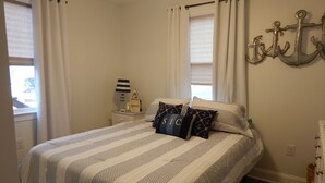 A bedroom with a bed, white curtains, a nightstand with a lamp, and a wall-mounted anchor decoration. - Newly renovated family home 11/2 blocks from the beach and town center (Sea Isle City)