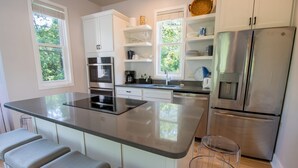 A modern kitchen with white cabinets, stainless steel appliances, and a large island with bar stools. - Luxury Beachwalk Resort House Closest to Beach includes resort amenities (Michigan City)