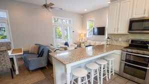 A kitchen with a granite countertop, white bar stools, a double oven, and a ceiling fan. - Luxury Beachwalk Resort House Closest to Beach includes resort amenities (Michigan City)