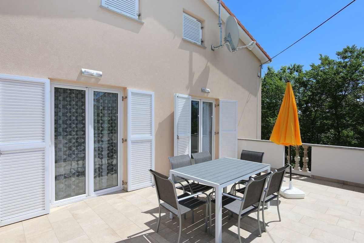 A balcony with a table and chairs, a sliding glass door, and an orange umbrella.