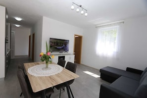 Uma sala de estar moderna com uma mesa de jantar de madeira, sofá preto e uma TV de tela plana.