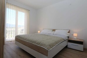 Quarto com cama, mesas de cabeceira e vista para o exterior.
