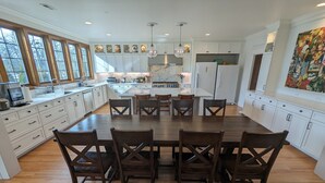 A spacious kitchen with white cabinetry, a large island, and a dining area with wooden chairs. - Luxurious newly constructed estate nestled in the quiet Talbot Hill neighborhood (Renton)