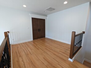 A spacious room with hardwood flooring, white walls, and a wooden door. - Luxurious newly constructed estate nestled in the quiet Talbot Hill neighborhood (Renton)