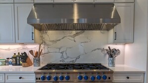 A kitchen with white cabinets, a stainless steel stove, and marble backsplash. - Luxurious newly constructed estate nestled in the quiet Talbot Hill neighborhood (Renton)