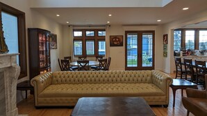 A spacious living room with a large beige sofa, a coffee table, and a fireplace. There are multiple windows providing natural light and a view of the outdoors. - Luxurious newly constructed estate nestled in the quiet Talbot Hill neighborhood (Renton)