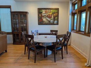 Un comedor con una mesa redonda, seis sillas, un aparador con puertas de cristal y un cuadro en la pared.