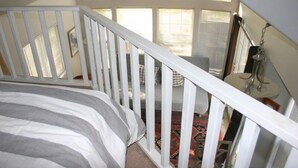 A bedroom with a bed, a white railing, a window, and a view of the outdoors.