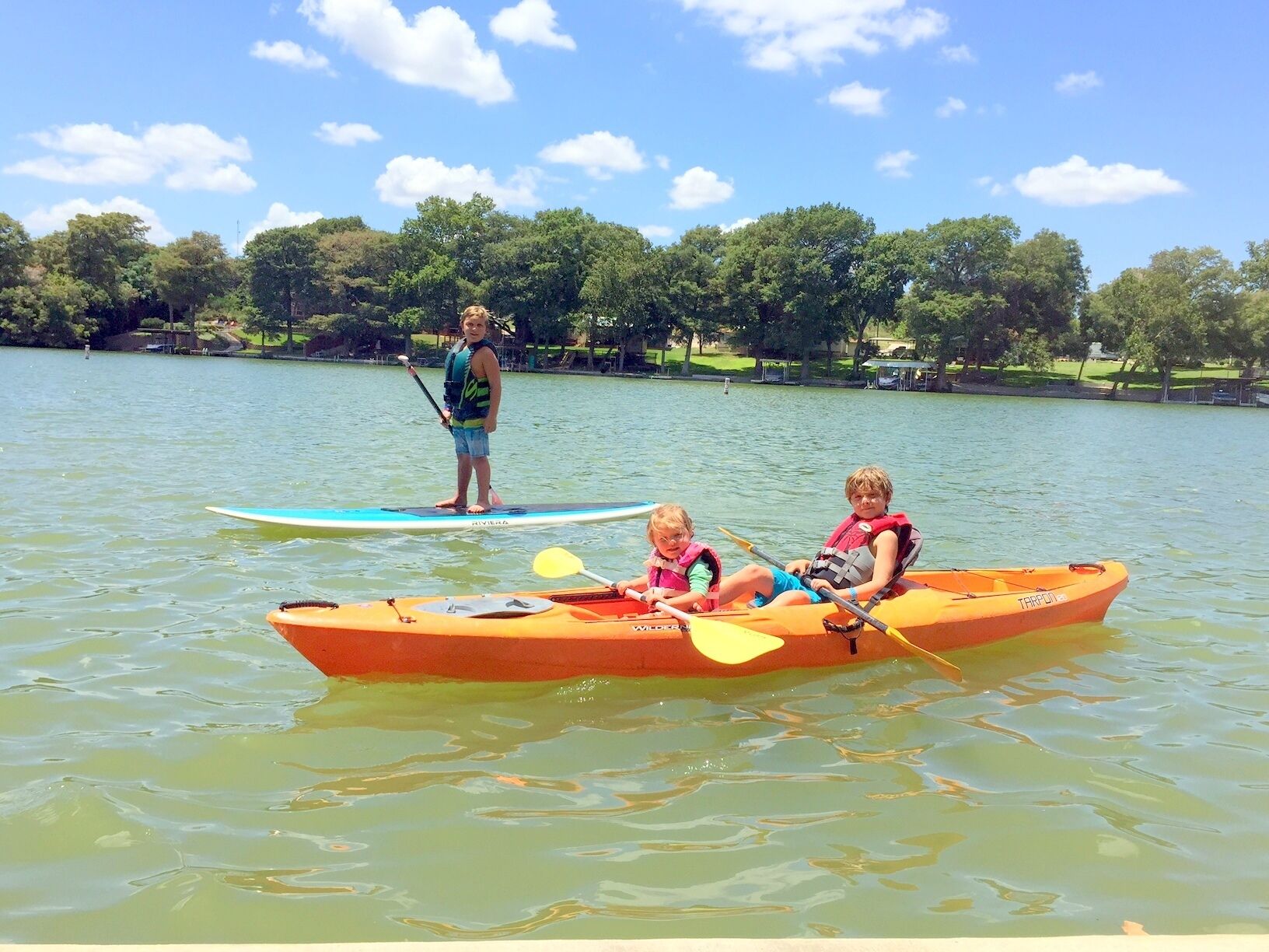 A calm lake with a paddleboarder and two kayakers.