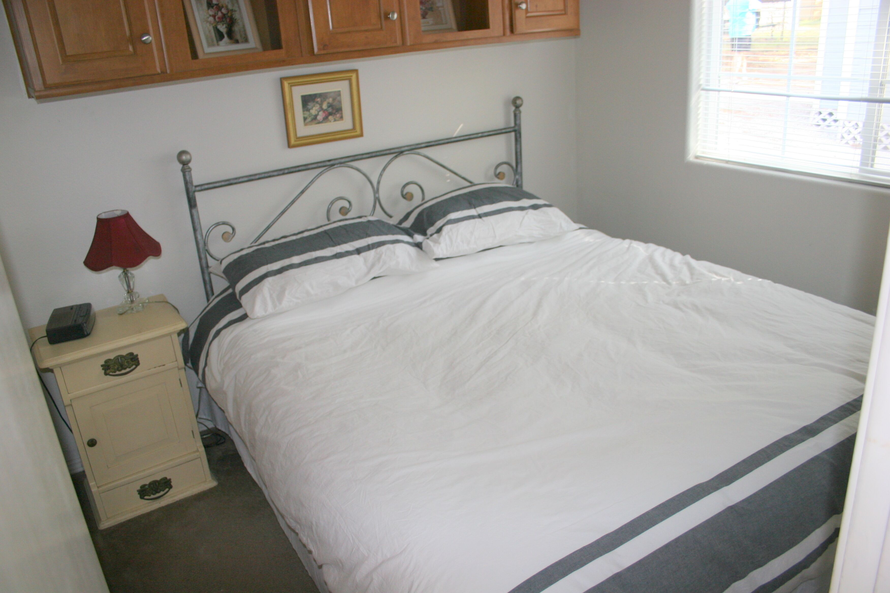 Een slaapkamer met een bed, nachtkastje, lamp en houten kasten.