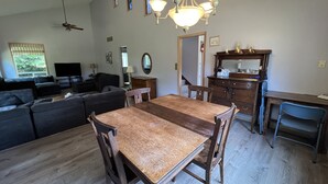 Ein Essbereich mit Holztisch und Stühlen, einem Deckenventilator, einem Fernseher und einem Fenster mit Jalousien.