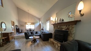 Ein geräumiges Wohnzimmer mit Kamin aus Stein, einem großen Ecksofa, einem runden Couchtisch und einem Essbereich im Hintergrund.