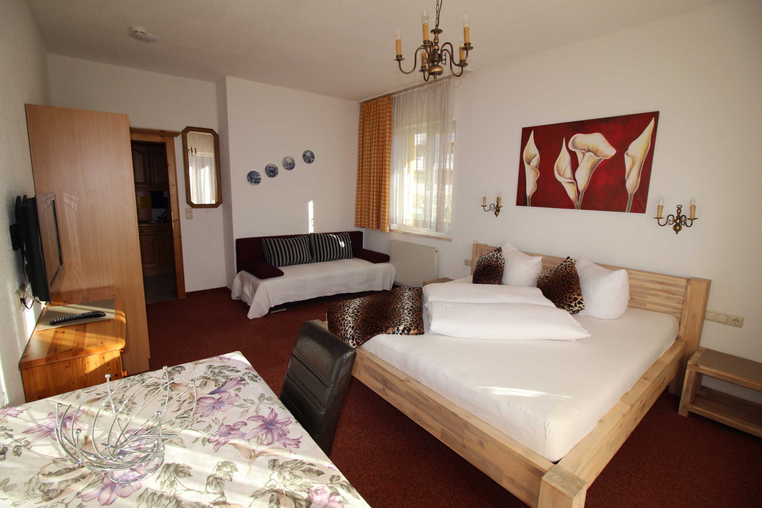 A hotel room with a bed, a sofa, a chair, a desk, and a mirror.