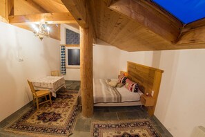 Un dormitorio acogedor con techo de madera, una cama con ropa de cama estampada, una mesita con una silla y una ventana con cortinas.