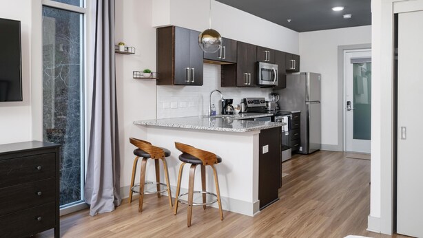 Eine moderne Küche mit dunklen Holzschränken, einem Edelstahlkühlschrank, einer Mikrowelle und einer großen Kücheninsel mit Barhocker.