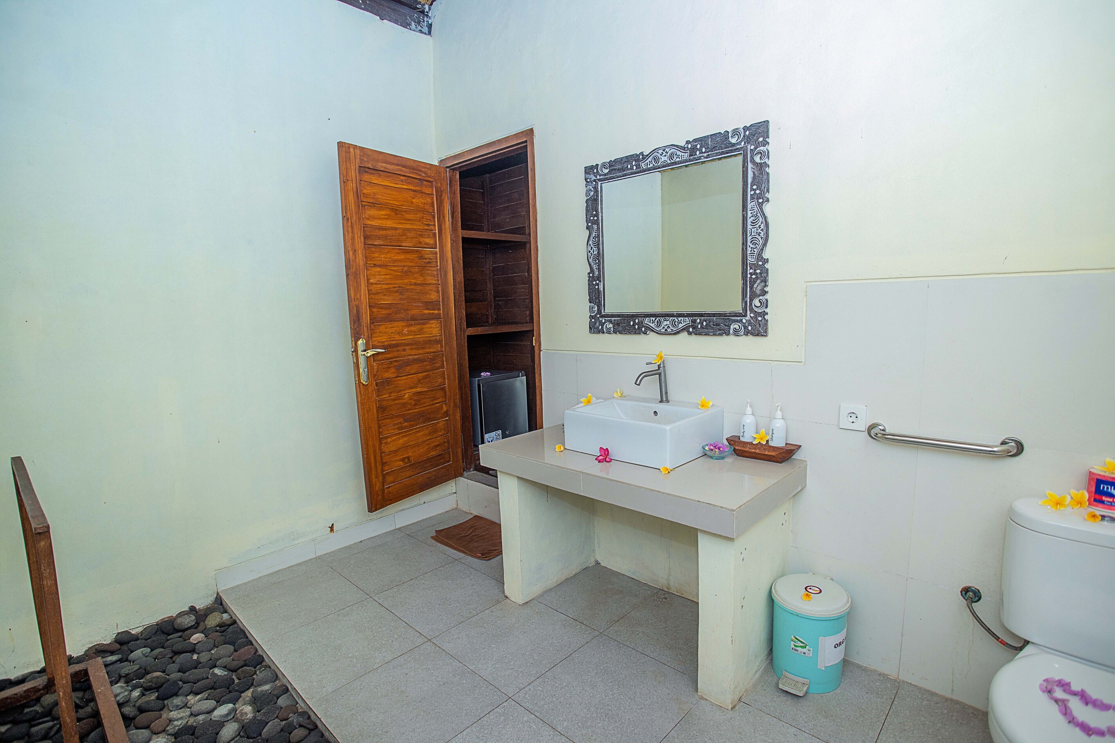 Ein Badezimmer mit Holztür, Waschbecken inklusive Spiegel und Toilette.