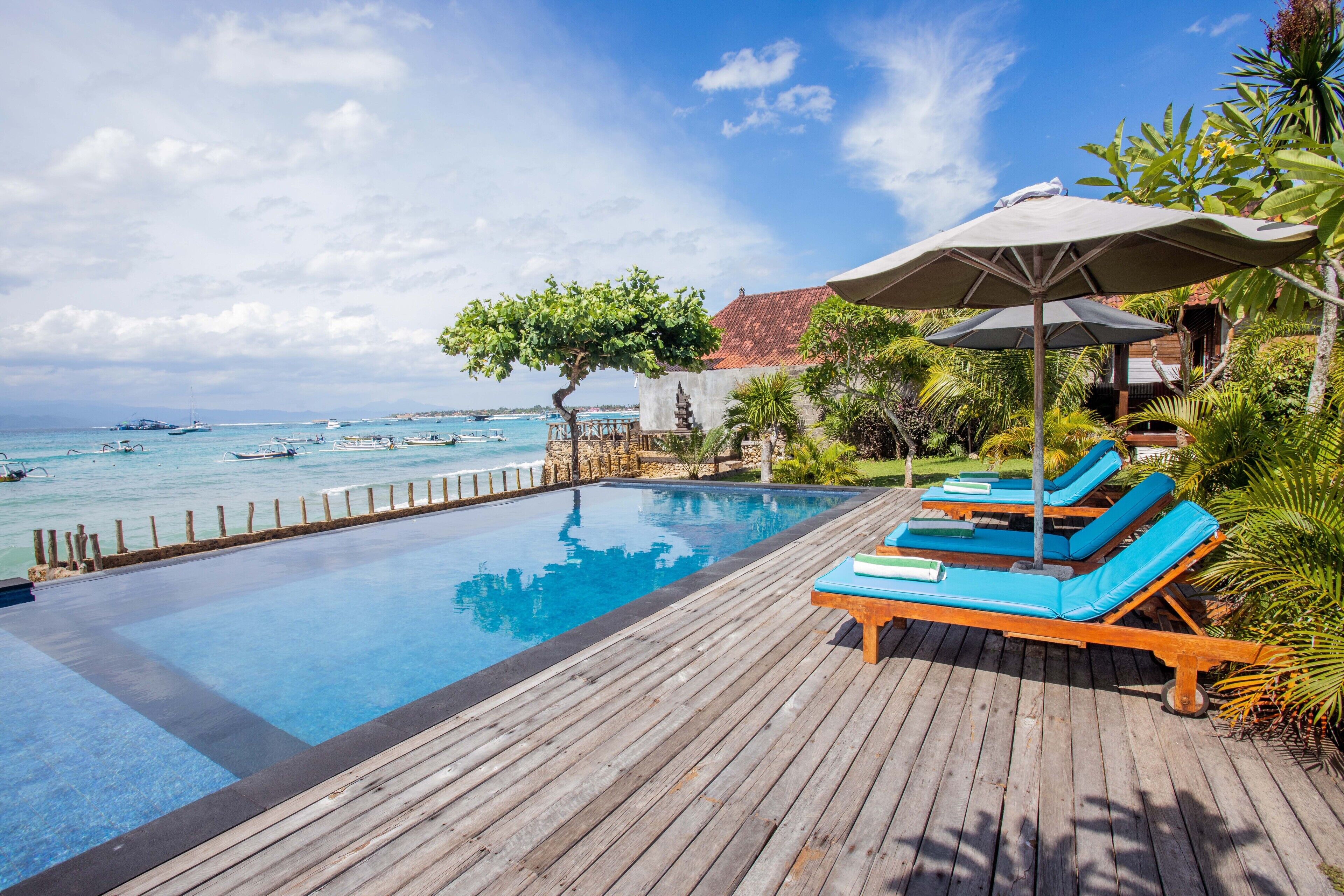 A wooden deck with a pool, lounge chairs, and umbrellas overlooking the sea.