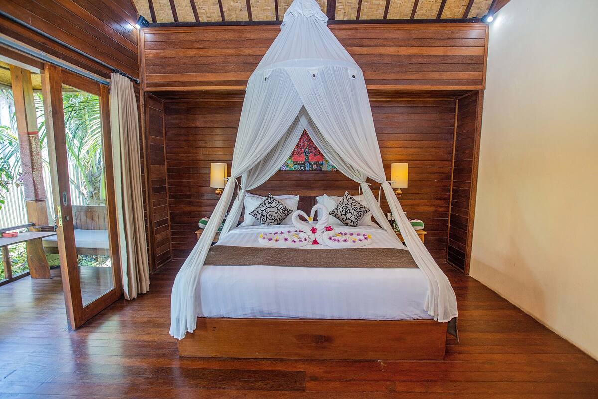 A wooden four-poster bed with a canopy, two bedside lamps, and a floral bedspread.