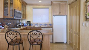 Una cocina con armarios de madera, un microondas, un refrigerador y dos sillas.