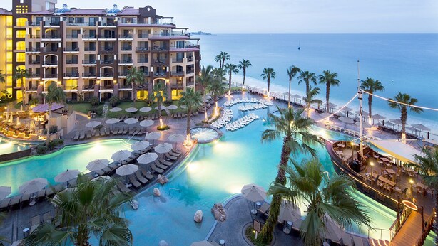 Un resort con varias piscinas, palmeras y vistas al océano.