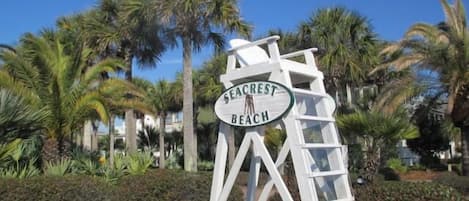Señal de Seacrest Beach con un diseño geométrico blanco y palmeras al fondo.