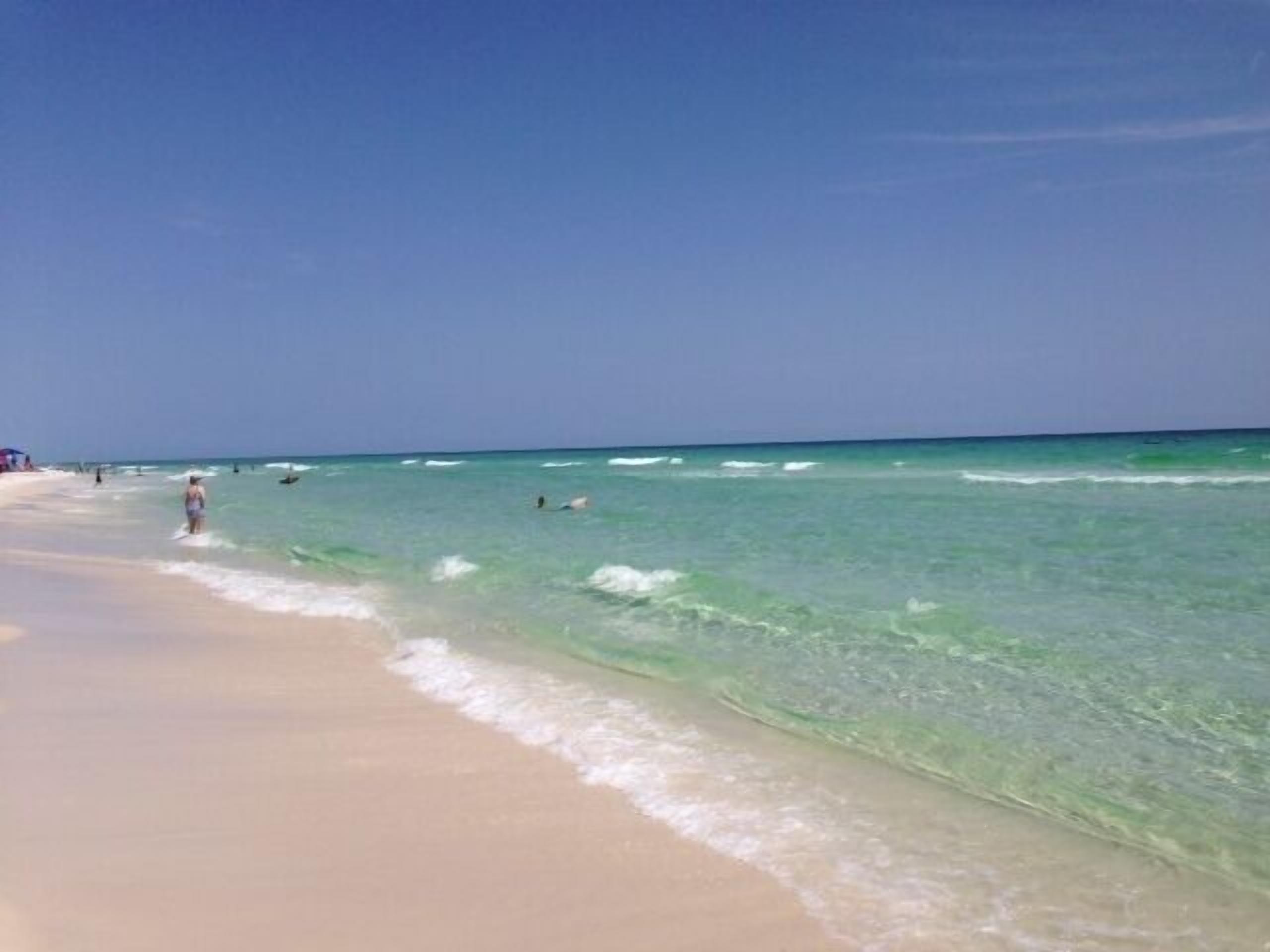 Una playa con agua turquesa cristalina, una orilla arenosa y algunas personas a lo lejos.