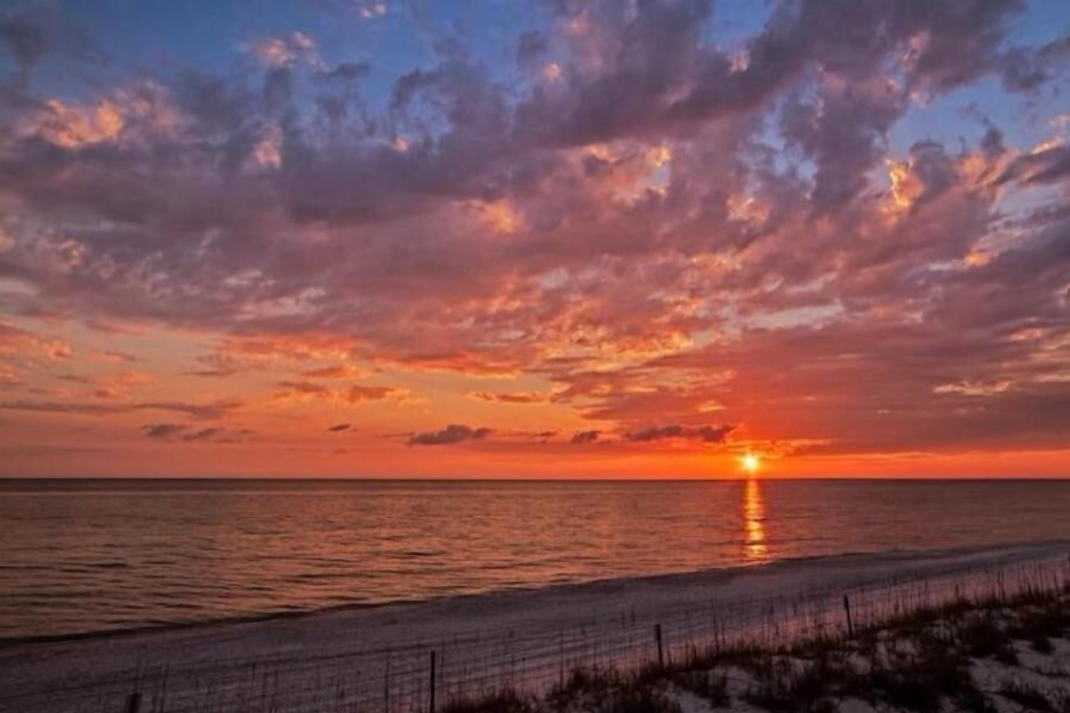 A sunset over a beach with a fence in the foreground.