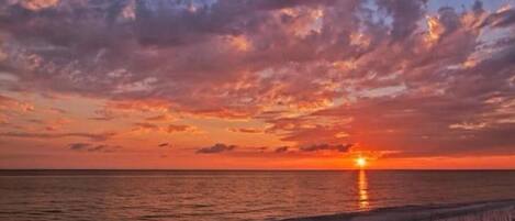 A sunset over a beach with a fence in the foreground.
