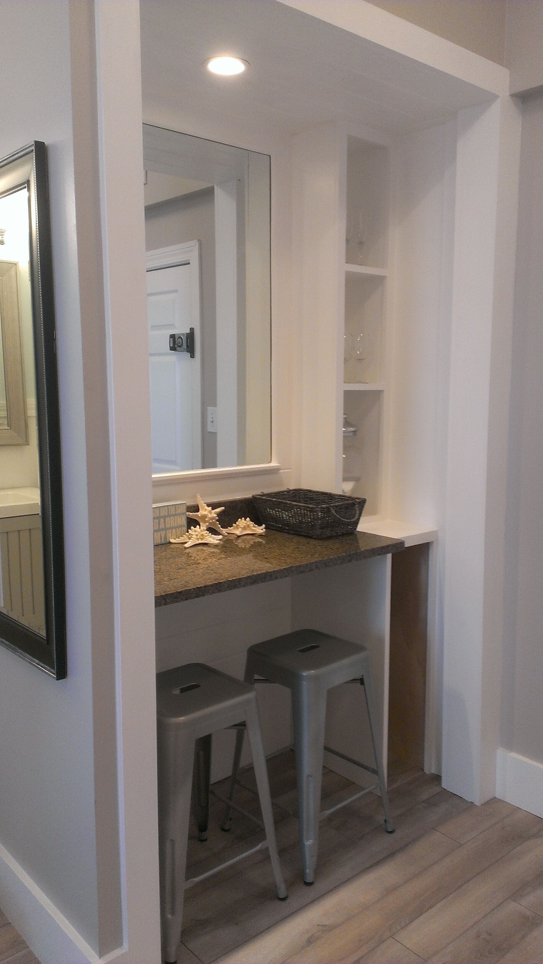 A bathroom with a vanity, mirror, two stools, and a shelf with glassware.