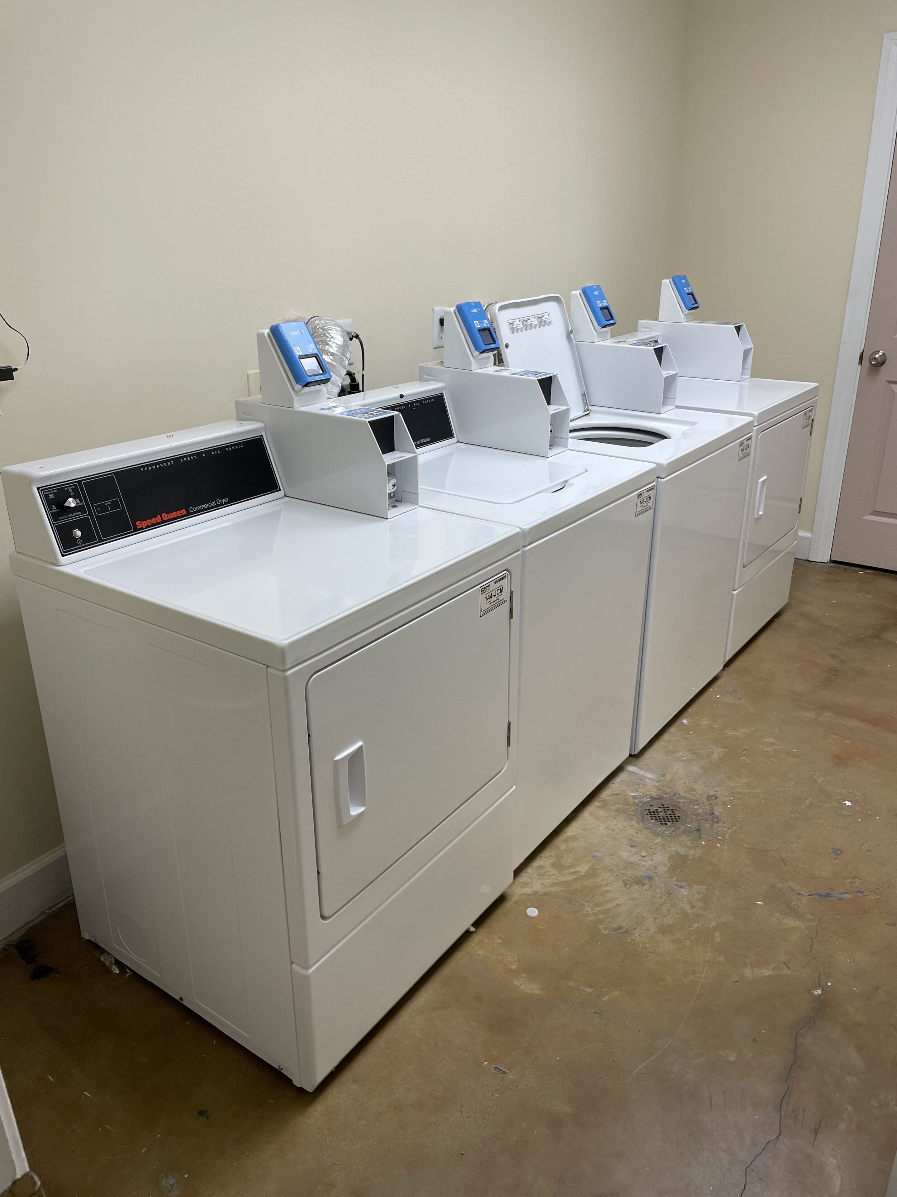 Een commerciële wasserij met meerdere wasmachines en drogers, een bedieningspaneel en een deur.